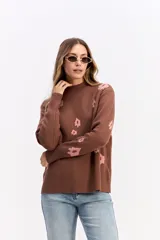 Sweater de tejido de punto color marrón con diseño estampado de flores en tonos rosados. Presenta cuello alto, mangas largas con puños ajustados y un corte relajado con terminación recta en la cintura.
