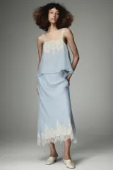 Top de estilo lencero color celeste, con escote recto y tirantes finos decorados con puntilla de encaje blanco. Presenta un detalle de encaje floral en el pecho.