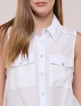 Camisa sin mangas de rayón texturado color blanco, de corte crop con cierre frontal de botones y lazos para anudar en el frente. Cuenta con cuello camisero, detalles de brillos en los hombros y bolsillos plaqué con solapa en el pecho.