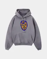 Canguro con capucha de corte regular, color gris con efecto stone wash. Presenta un estampado frontal de una máscara de luchador en tonos azul y naranja, con el logo de la marca debajo. Incluye bolsillo tipo canguro y puños acanalados.