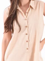 Monoprenda corta sin mangas, color beige, con cuello camisero y cierre frontal de botones. Presenta un corte holgado y relajado.