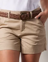 Short de jean azul oscuro con tiro medio, cierre frontal con botón y pasadores para cinturón. Incluye un cinturón trenzado de cuero sintético color marrón con hebilla circular metálica.
