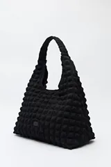 Cartera tipo hobo o tote bag negra con textura acolchada y efecto tridimensional. Presenta un asa fruncida y un diseño blando.