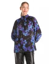 Blusa de gasa plisada con estampado floral en tonos azules y violetas sobre fondo negro. Presenta cuello alto, mangas largas con puños abotonados y un diseño fluido con textura plisada.