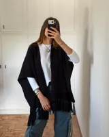 Ruana de tejido de punto en color negro, con diseño abierto, corte holgado y terminación con flecos en el ruedo.