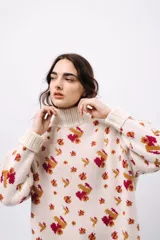 Polera de tejido de punto con cuello alto, diseño holgado y estampado jacquard con motivos geométricos y figuras en tonos beige, naranja y celeste.
