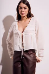 Blusa blanca de algodón con escote en V, mangas largas con detalles de encaje y cierre frontal con lazos.