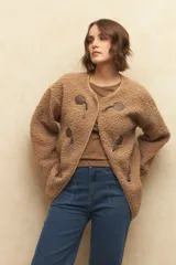 Abrigo gamulán de corderito color crudo, con alamares de cuero sintético negro y cierres metálicos.