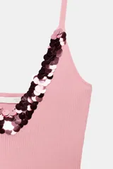 Top rosado de punto con escote en V y tirantes finos, adornado con una aplicación de lentejuelas brillantes alrededor del escote.