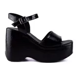 Sandalias negras de plataforma con taco corrido, tira ancha sobre los dedos y pulsera al tobillo con hebilla metálica.