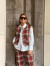 Chaleco de corte recto con estampado de cuadros en tonos rojos y marrones, con cierre frontal de botones y bolsillos laterales.