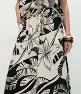 Pollera larga (midi) de corte evasé, con cintura elástica y lazo. Presenta un estampado grande en blanco y negro de motivos tropicales como hojas de palmera y flores.