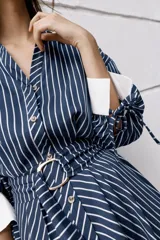 Vestido midi azul marino con rayas blancas, cuello solapa, escote en V y cierre frontal con botones. Cuenta con mangas abullonadas por debajo del codo con puños anchos a contraste, cinturón ajustable del mismo tejido con hebilla metálica y falda evasé.