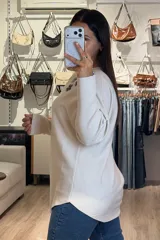 Buzo tejido de punto en color beige, con diseño de flores aplicadas en tono gris oscuro y detalles de brillos plateados que irradian desde las flores. Presenta cuello redondo amplio, mangas largas con caída holgada y corte recto.