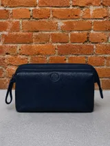 Necessaire de cuero azul marino con textura granulada, cierre superior y logo circular grabado en el centro.