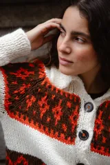 Saco tejido a mano con diseño jacquard en tonos rojo, naranja y marrón. Presenta cuello tipo polo, cierre frontal con botones grandes, mangas largas y tajos laterales en el ruedo.