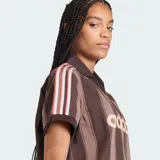 Camiseta de fútbol Adidas de manga corta, color marrón con diseño de rayas verticales oscuras. Presenta cuello polo con escote en V, el logo clásico de la marca bordado en el pecho junto con la inscripción "adidas" en gran tamaño al frente, y las franjas características de la marca en los hombros.