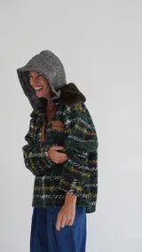 Buzo canguro oversize de paño de lana gris con capucha estampada y cuello de corderito blanco. Cuenta con aberturas laterales en el ruedo y detalles de cuero sintético marrón en el cierre frontal y etiqueta.
