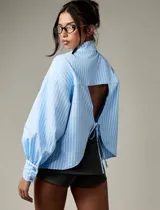 Camisa de rayas verticales celestes y blancas, con cuello clásico, mangas largas abullonadas con puños abotonados y espalda abierta con lazo regulable.