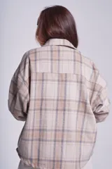 Sobrecamisa de franela color beige con estampado a cuadros en tonos marrones y azules, de corte holgado, con cuello clásico, cierre abotonado y bolsillos delanteros con solapa.