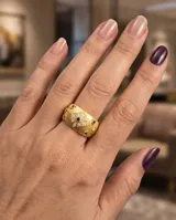 Anillo ancho de bronce con baño de oro, acabado texturizado y diseño con flor central incrustada de circonias blancas y una circonia azul en el centro.