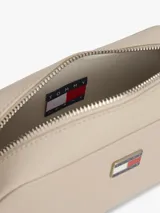 Cartera tipo bandolera Tommy Jeans de diseño compacto y acabado liso en color beige. Cuenta con cierre de cremallera superior y una insignia metálica distintiva de la marca en la parte frontal.