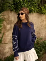 Buzo blanco de jogging sin friza, con cuello redondo y bordado floral marrón en las mangas.