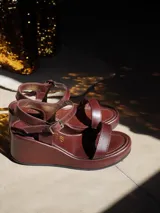 Sandalias de plataforma con taco cuña color marrón y tiras doradas metalizadas en el empeine y el talón. Cuentan con tira ajustable con hebilla metálica en el tobillo.