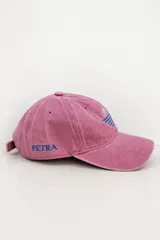 Gorro tipo gorra bordó con efecto gastado, visera curva y diseño de seis paneles con ojales de ventilación bordados. Presenta un bordado frontal minimalista en fucsia que representa un sol sobre el horizonte y detalles de texto bordados en el lateral.