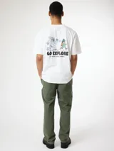 Remera blanca de corte oversize con estampado gráfico en la espalda que muestra una escena humorística de un yeti persiguiendo a una persona junto con la leyenda "GO EXPLORE".
