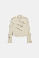 Chaqueta corta de estilo militar con cuello alto y manga larga. Confeccionada en tejido jacquard con diseño floral, presenta botones metálicos en relieve en el cierre frontal, hombros y puños. Incluye trabillas en los hombros, forro interior y acabados desflecados.