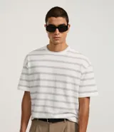 Remera de corte boxy con cuello redondo y mangas cortas. Presenta un diseño de rayas horizontales finas en tonos gris sobre fondo blanco.