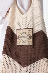 Bolso tejido a crochet con diseño a rayas horizontales en tonos marrón y beige. Tiene un parche cuadrado con el texto "Flowers Petra Club" y asas de hombro.