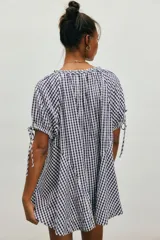 Túnica de algodón liviano con estampado de cuadros vichy en color azul marino y blanco. Presenta caída amplia y largo extendido, escote redondo con botonadura frontal y mangas cortas abullonadas con lazos ajustables.