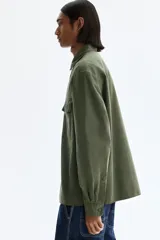 Camisa cargo color verde militar de corte regular, confeccionada en tejido ripstop de algodón. Cuenta con cuello inglés, cierre frontal de botones, bolsillos con solapa en el pecho y mangas largas con puños abotonados.