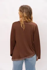 Blusa de tela elastizada color marrón, con corte asimétrico, mangas anchas y detalle de puntilla en el ruedo.