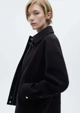 Chaqueta oversize de tejido mezcla de lana en color negro, con cuello camisero, cierre frontal de cremallera oculta, bolsillos laterales y mangas largas con puños abotonados.