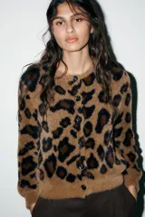 Chaqueta de punto con textura suave, cuello redondo y manga larga. Presenta un diseño de estampado animal print en tonos marrones y negros, con cierre frontal de botones.