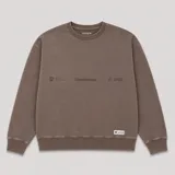 Buzo de cuello redondo en color marrón con efecto lavado, presenta un pequeño estampado gráfico en el pecho y una etiqueta decorativa en el ruedo.
