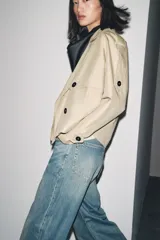 Trench corto negro confeccionado en hilatura con mezcla de algodón. Cuello solapa de muescas ajustable con trabilla y botones. Manga larga. Bolsillos delanteros. Detalle de trabillas en hombros. Cierre frontal cruzado con botones.