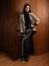 Blazer de corte clásico color beige, con solapa, hombreras y detalle de encaje negro en los puños y el ruedo. Presenta falsos bolsillos frontales y una textura similar al terciopelo.