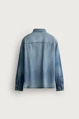 Camisa relaxed fit confeccionada en denim ligero de algodón, con cuello solapa, manga larga con puño abotonado, dos bolsillos de parche en el pecho con solapa y cierre frontal de botones. Presenta un efecto de lavado desgastado.