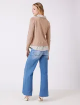 Buzo de punto fino color beige con diseño de camisa incorporada. Presenta escote en V con cierre frontal de botones, mangas largas con puños acanalados y cuello y ruedo con estampado de rayas verticales que simulan una camisa debajo.