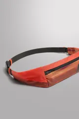 Riñonera deportiva técnica de color gris y negro, confeccionada en tejidos técnicos. Posee un compartimento principal con cierre de cremallera, bolsillos laterales planos (uno con mosquetón para llaves) y asa ajustable con hebilla de liberación rápida.