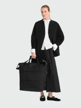 Bolso de viaje grande de la línea Le Pliage de Longchamp, color negro, con diseño ampliable, asas cortas y correa ajustable para el hombro.