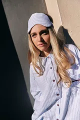 Pijama de dos piezas de algodón a rayas celestes y blancas, compuesto por una camisa de manga larga con botones y ribetes marrones, y un pantalón largo de corte recto con elástico en la cintura.