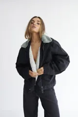 Campera bomber de denim azul oscuro con costuras a contratono en color verde. Presenta cuello de corderito en color marrón, cierre frontal y diseño holgado.