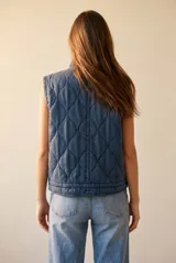 Chaleco acolchado de algodón en color azul lavado, con cierre frontal de cremallera y botones a presión, cuello alto y bolsillos frontales.