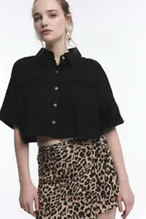 Camisa crop de manga corta en color crudo, con cuello camisero, cierre frontal de botones y dos bolsillos con solapa en el pecho.