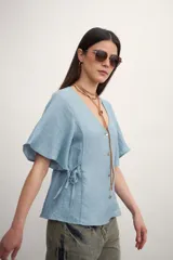 Camisa negra con botones dorados, escote en V y mangas cortas amplias con lazos laterales. 